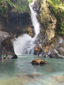 When is the best time to visit Panama? A child standing in a swimming suit in front of a big waterfall with turquoise water. Waterfall will be the most beautiful during the rainy season. You can do waterfall hikes year-round with Istmo Retreat & Adventures.