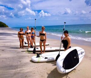 Women with stand-up paddleboards on a quiet beach in Panama with Istmo Retreat & Adventures, enjoying one of the best family vacation destinations.