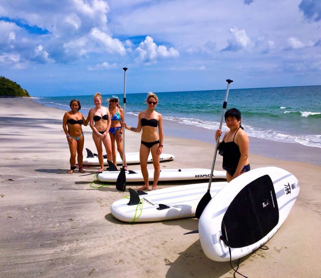 sup-beach-panama-best-family-vacation-destination Women with stand-up paddleboards on a quiet beach in Panama with Istmo Retreat & Adventures, enjoying one of the best family vacation destinations.