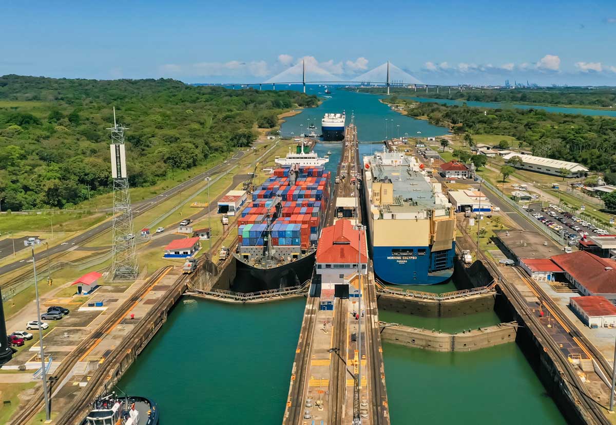 View of ships passing through the locks at the Panama Canal near Panama City, with lush rainforest and bridge in the background. Panama Canal locks demonstrating engineering adapted to geological features of the Continental Divide